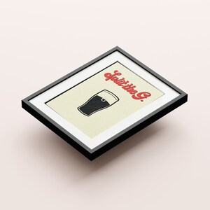 May include: Framed art print featuring a black pint glass illustration with the text "Split the G." in red. The artwork is set against a cream background, encased in a black frame, and angled slightly.