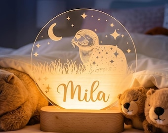 May include: A personalized night light with a sloth design, the name "Mila", and a crescent moon and stars. The lamp sits on a wooden base and is surrounded by plush bear toys. The image also includes the text "Made in USA".