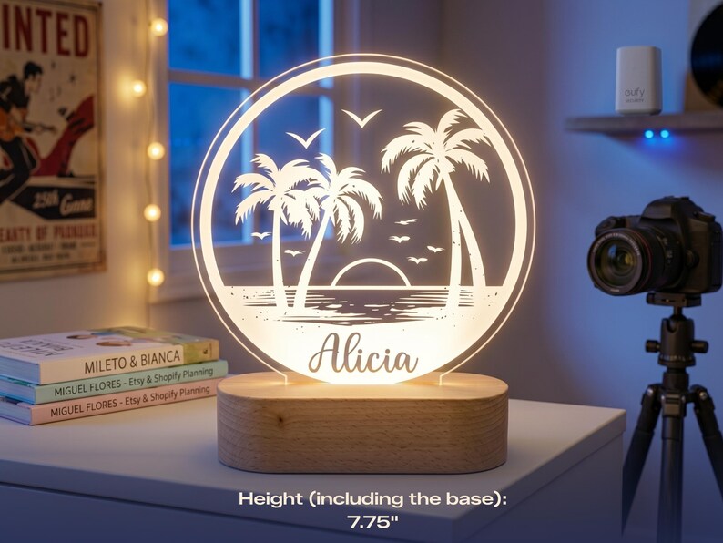 May include: A personalized LED night light featuring a beach scene with palm trees, seagulls, and a sunset. The name "Alicia" is displayed below the image. The light sits on a wooden base and measures 7.75 inches in height.
