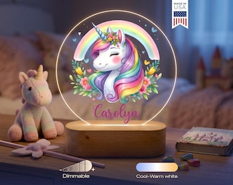 May include: A circular LED night light featuring a colorful unicorn illustration with a rainbow, flowers, and the name Carolyn printed in purple script. The light is mounted on a rectangular wooden base and includes dimmable cool-warm white settings.