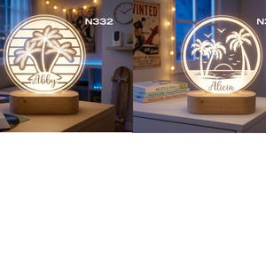 May include: Two illuminated wooden base lamps with a circular design. One features palm trees and the name "Abby", the other has palm trees, birds, and the name "Alicia". Both lamps are lit with a warm glow, creating a decorative and personalized touch.
