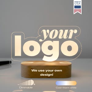 May include: A lighted sign with the text "your logo" in a stylized font, illuminated against a neutral background. The sign sits on a wooden base, with the text "We use your own design!" below. Features include dimmable light and cool-warm white options. Made in USA.