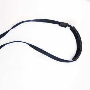 May include: A black and navy blue eyeglass strap with a curved, padded neck rest. The strap is made of a woven material and has two black plastic connectors. The strap is designed to hold eyeglasses.