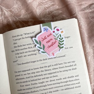 Op de afbeelding: Een roze bladwijzer met de tekst "Just one more chapter!" in witte letters. De bladwijzer heeft een bloemmotief met vlinders en groene bladeren.