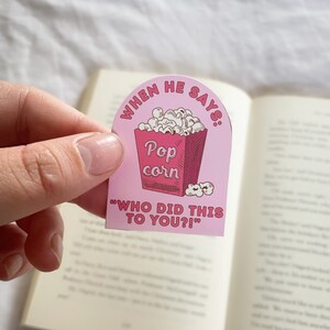 Op de afbeelding: Roze en rode bladwijzer met een cartoonillustratie van een popcorn emmer en de tekst "When he says: Pop corn "Who did this to you?!""