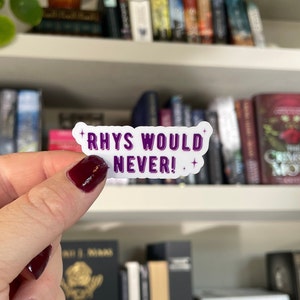 Può includere: Un adesivo bianco con testo viola che dice "Rhys non lo farebbe mai!" con una piccola stella su ogni lato. L'adesivo è tenuto da una mano con smalto rosso.
