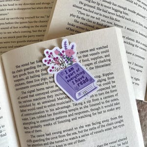 Peut inclure: Un marque-page en forme de livre violet avec le texte "I am a part of everything I have read" et un motif floral. Le marque-page est placé sur un livre ouvert avec du texte.
