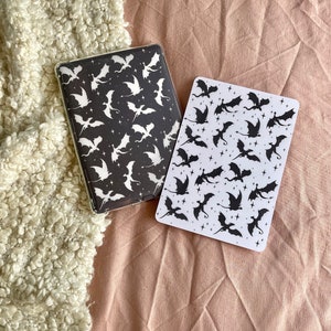 May include: Two black and white dragon patterned covers for a journal or planner. The covers are on a light brown surface.