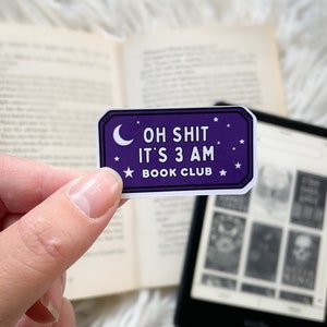 Op de afbeelding: Paarse sticker met witte tekst en sterren die "Oh Shit It's 3 AM Book Club" zegt.