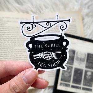 Op de afbeelding: Zwart-witte sticker van een ketel met een skelet hand die een kopje thee vasthoudt. De tekst luidt "The Suriel Tea Shop".