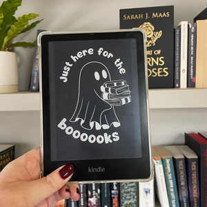 May include: A white ghost holding a stack of books with the text "Just here for the boooooks" on a black background. The image is on a Kindle e-reader.