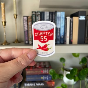 Può includere: Un adesivo con un design a forma di lattina con la scritta "CAPITOLO 55" in rosso e due peperoncini rossi. Le parole "EXTRA PICCANTE" sono sotto. L'adesivo è tenuto in mano.