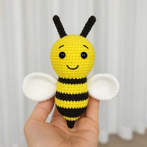 May include: A crocheted bee toy with black and yellow stripes, white wings, and a smiling face.