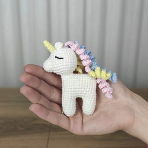 May include: A white crocheted unicorn with a yellow horn and a multi-colored mane. The mane is pink, blue, and yellow.
