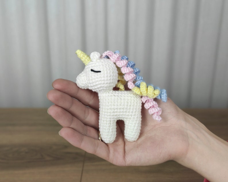 May include: A white crocheted unicorn with a yellow horn and a multi-colored mane. The mane is pink, blue, and yellow.