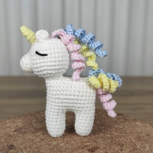 May include: A white crocheted unicorn with a pink, yellow, and blue curly mane and tail.