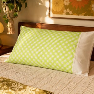 Peut inclure: Une taie d'oreiller rectangulaire présentant un motif à carreaux vichy vert citron vif et blanc sur le corps principal, contrasté par un panneau en tissu blanc uni sur le côté droit. La taie est posée sur un lit avec un couvre-lit blanc texturé.