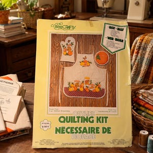 Peut inclure: Un kit de piquage BeeCrafty pour un ensemble de cuisine de 3 pièces comprenant un tablier, une manique et un dessous de plat imprimés avec des motifs d'oranges. L'emballage jaune porte le texte Fresh Fruit, Outline Quilting Kit et style Q 5011.