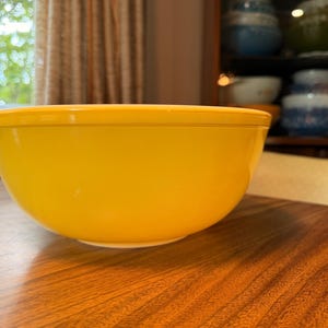 Peut inclure: Un bol mélangeur jaune vif uni avec un extérieur lisse et arrondi et une large ouverture sur le dessus. Le bol présente un design simple et épuré avec une couleur uniforme sur toute la surface extérieure, illustrant une forme de cuisine classique.