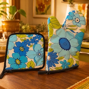 May include: A square quilted pot holder and a matching oven mitt featuring a vibrant floral pattern in shades of blue, light blue, and lime green on a white background. Both kitchen accessories are finished with a solid black fabric trim.