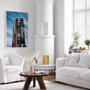 May include: A white living room with a white tiled fireplace, a white couch, and a white coffee table. A framed print of a red double-decker bus hanging on the wall.