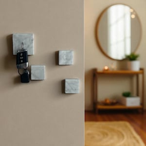 Peut inclure: Ensemble de quatre porte-clés carrés en marbre, montés sur un mur beige. L'un d'eux porte un jeu de clés de voiture. Le marbre présente un veinage blanc et gris. Un élément de décoration intérieure moderne.