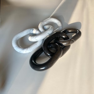 Könnte beinhalten: Dekorative Kettenglieder aus Marmor in Weiß und Schwarz. Die weißen Glieder haben ein Marmormuster, während die schwarzen Glieder einfarbig sind. Die Glieder sind ineinander verschlungen und bilden eine moderne Skulptur. Der Hintergrund ist neutral.