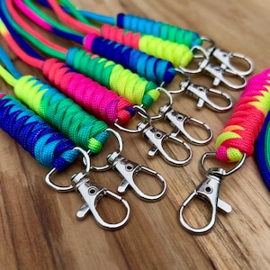May include: A collection of colorful lanyards with metal swivel clasps. The lanyards are made of braided cord in vibrant rainbow hues, including pink, blue, green, and yellow. The clasps are silver-toned and attached to the ends of the cords.