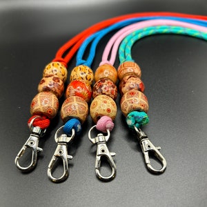 May include: Four colourful beaded lanyards with metal clasps. The beads are wooden and have intricate patterns. The lanyards are red, blue, pink, and green.