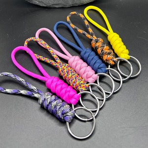 Puede incluir: Un conjunto de siete llaveros coloridos hechos con paracord trenzado. Cada llavero tiene una combinación de colores diferente y un anillo de llave plateado.