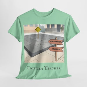 May include: Mint green t-shirt with a graphic featuring a cracked paving slab, a "Keep Off" sign, and directional signs reading "World's Biggest" and "Paving Slab." The text "English Teacher" is printed at the bottom.