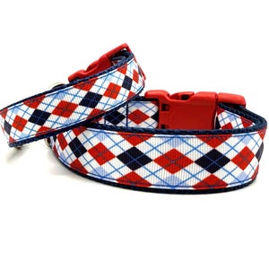 Puede incluir: Dos collares para perros con un patrón de rombos rojo, blanco y azul. Los collares tienen una hebilla de plástico roja y un ribete azul oscuro. El patrón de rombos consiste en diamantes rojos, azul marino y azul claro.