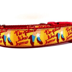 May include: Red dog collar with a yellow and red ribbon featuring the text "No place like home" and a graphic of ruby slippers.