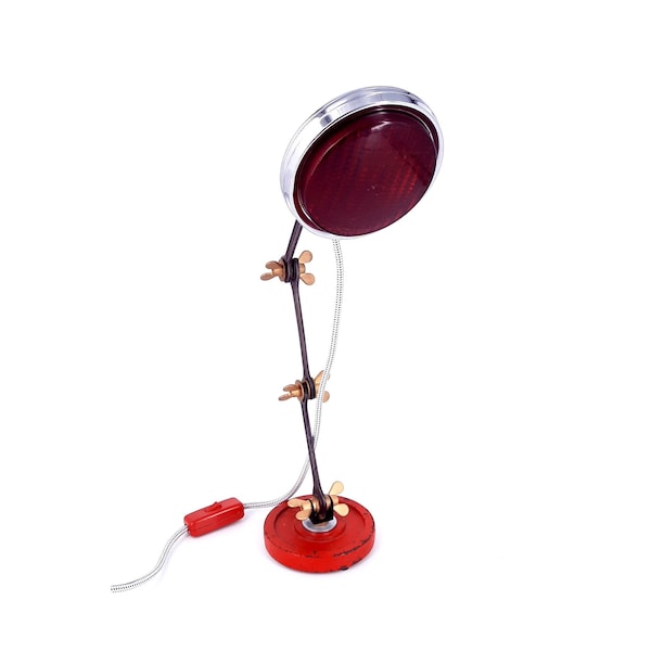 Lampe de table surcyclée à partir d'un vieux phare rouge et d'un poids avec un bras pivotant fait de clés et de boulons ailés.