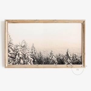 Può includere: Una fotografia incorniciata di una scena di foresta innevata. Gli alberi sono coperti di neve e il cielo è di un azzurro pallido e morbido. L'immagine è incorniciata in una cornice di legno chiaro.