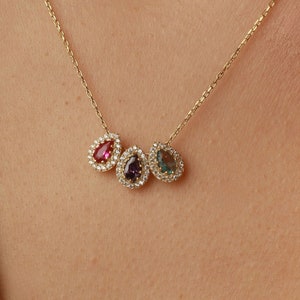 May include: A gold chain necklace with three teardrop-shaped pendants. Each pendant is set with a different coloured gemstone and surrounded by a halo of smaller diamonds.