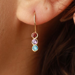 May include: Gold dangle earrings with three gemstones: red, purple, and blue.