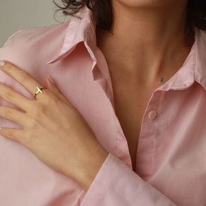May include: A gold cross ring on a finger. The ring is simple and minimalist.