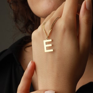 以下が含まれることがあります： 金のチェーンネックレスに金のEの文字のペンダントが付いている。