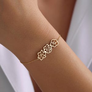 May include: A delicate gold chain bracelet with three cutout flower charms. The flowers are arranged in a row and are connected by a thin chain.