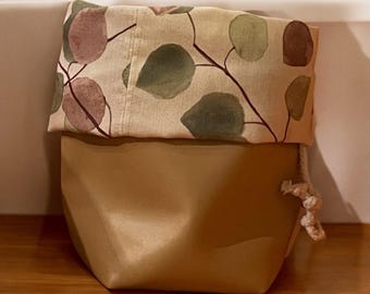 May include: A brown fabric storage bin with a drawstring closure. The bin has a removable lid with a leafy pattern in shades of green, brown, and pink.