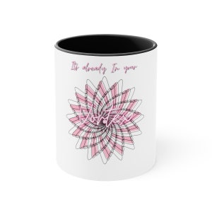 May include: White ceramic coffee mug with a black interior. The mug features a pink and black floral design with the words "It's already in your Vortex" in pink script.