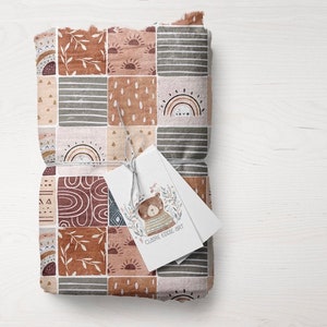 May include: A brown and beige fabric with a patchwork design featuring rainbows, suns, and geometric shapes. A small tag with a bear illustration and the text "CLAIRE EDDIE ART" is attached to the fabric.