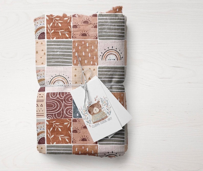 May include: A brown and beige fabric with a patchwork design featuring rainbows, suns, and geometric shapes. A small tag with a bear illustration and the text "CLAIRE EDDIE ART" is attached to the fabric.
