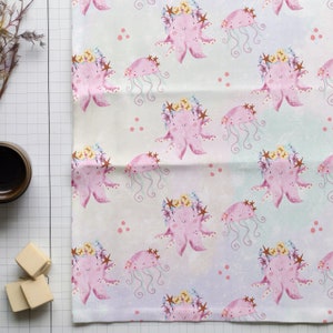 May include: A white fabric with a repeating pattern of pink octopus with floral crowns and blue jellyfish. The background has a light pink and blue watercolor effect with small pink dots.