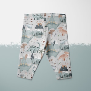 Puede incluir: Leggins grises con estampado de dinosaurios y monta&ntilde;as. El estampado presenta colores azul, verde, marr&oacute;n y naranja. Los leggins tienen un fondo blanco.