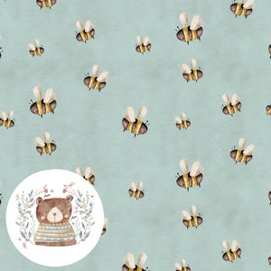 Op de afbeelding: Een lichtblauwe achtergrond met een herhalend patroon van gele en zwarte bijen. Een witte cirkel met een bruine beer die een gestreepte trui draagt, bevindt zich in het midden van de afbeelding.