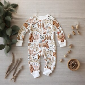 May include: White baby onesie with a zipper closure and a woodland animal print. The print features squirrels, rabbits, birds, and mushrooms in brown and beige tones.