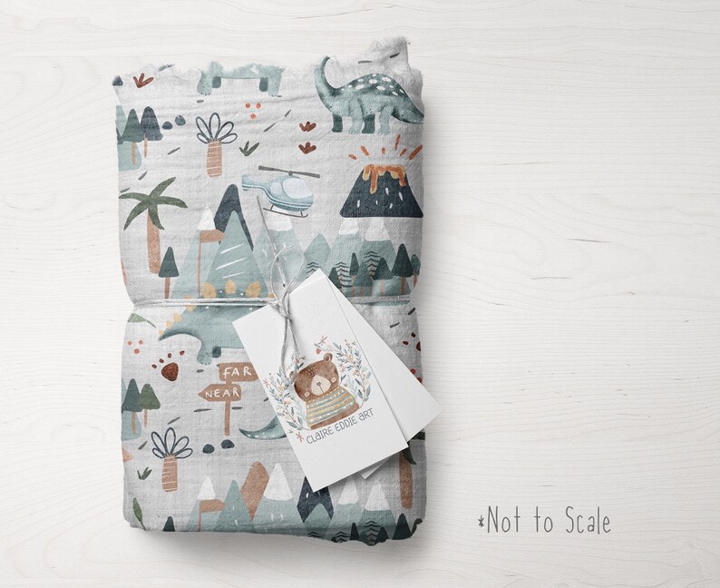 Puede incluir: Una manta de muselina gris y blanca con estampado de dinosaurios, monta&ntilde;as y palmeras. La manta est&aacute; doblada y atada con una etiqueta blanca que dice "Claire Eddie Art" y "Far Near".