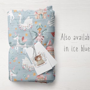 May include: A blue fabric with a whimsical pattern featuring unicorns, fairies, swans, stars, and castles. The fabric is folded and tied with a white tag that says "Claire Eddie Art". The text "Also available in ice blue" is written in black on a white background.
